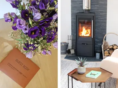 a living room with a fireplace and a bouquet of purple flowers at Long House, Boskensoe Barns in Helford Passage