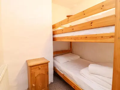 a bunk bed room with two bunk beds and a table at Threshings Cottage in Tintagel