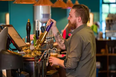 a man with a beard standing behind a bar with a drink at County Arms in Truro