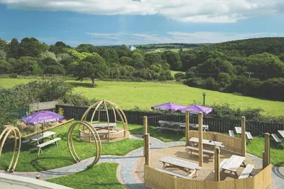 a playground with benches and tables and purple umbrellas at County Arms in Truro