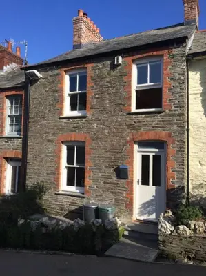 a brick house with a white door and two windows at Fernleigh Cottage in Boscastle