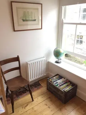 a room with a chair and a window and a basket of books at Fernleigh Cottage in Boscastle