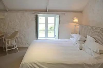 a bedroom with a large white bed with a window at Bonython Farmhouse in Cury