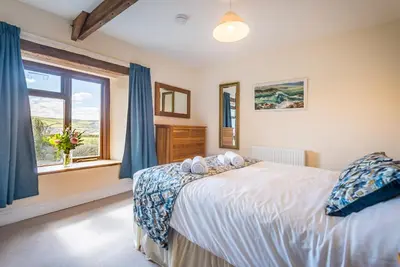a bedroom with a bed with blue curtains and a window at Cargurra Park Farm in Boscastle