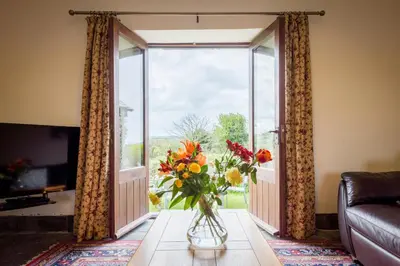 a vase of flowers on a table in front of a window at Cargurra Park Farm in Boscastle