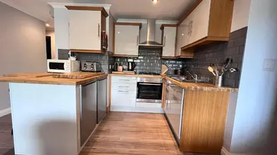 a kitchen with white cabinets and wooden floors at Beachcombers Apartments in Newquay