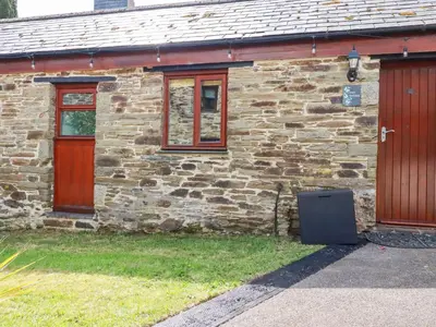 a stone house with red doors and a trash can outside at Cosy Cottage in Liskeard