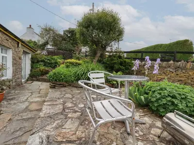 a patio with a table and chairs on a stone patio at The Garden Apartment in Tintagel