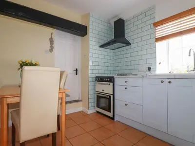 a kitchen with white cabinets and a table and a stove at The Garden Apartment in Tintagel