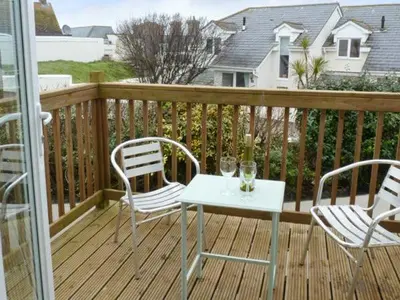 a wooden deck with two chairs and a table with wine glasses at Beachcombers in Newquay