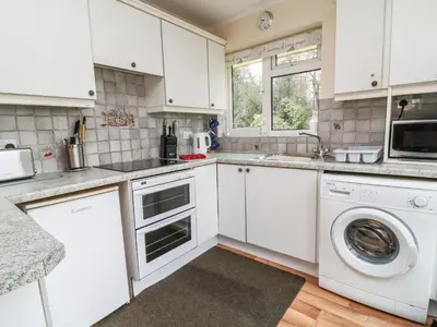 a kitchen with white cabinets and a washer and dryer at Peacehaven in Liskeard