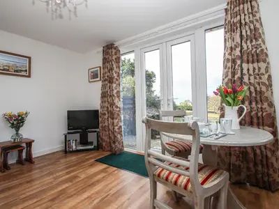 a living room with a table and a large window at Sunset Cottage in Tintagel