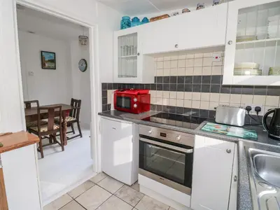 a kitchen with white cabinets and a red appliance on the counter at Driftwood in Wadebridge