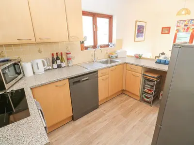a kitchen with wooden cabinets and a stainless steel refrigerator at Kernow Cottage in Helston