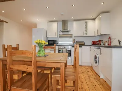 a kitchen with a wooden table and chairs and a kitchen with white cabinets at Vine Cottage in Saint Ewe