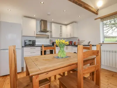 a kitchen with a wooden table with chairs and a vase of flowers at Vine Cottage in Saint Ewe