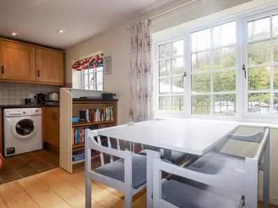 a kitchen with a white table and some windows at Honeysuckle in Gorran Haven