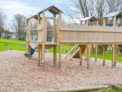 a wooden playground with a slide in a park at High Tide in Wadebridge