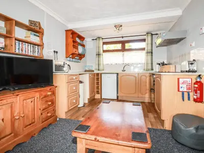 a kitchen with wooden cabinets and a tv and a table at Stable Cottage in Newquay