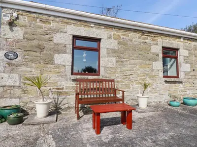 a wooden bench sitting in front of a stone building at Stable Cottage in Newquay