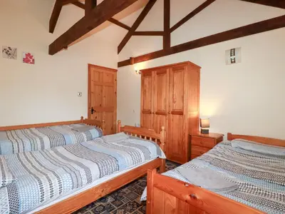 two beds in a bedroom with wooden cabinets at Kingfisher Barn in Liskeard