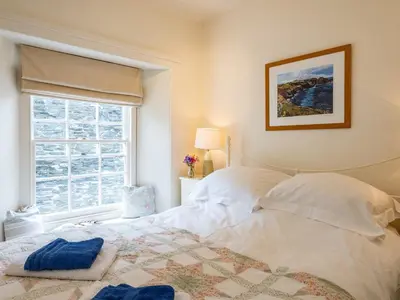 a bedroom with a white bed and a window at Cobble Cottage in Boscastle