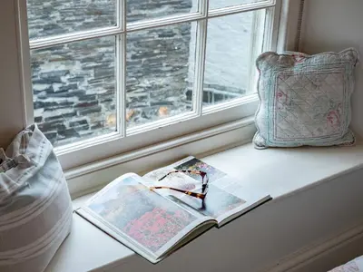 a book on a window sill with a pillow and a book at Cobble Cottage in Boscastle