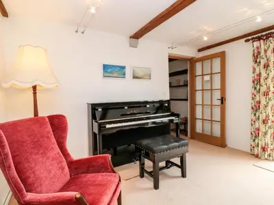 a living room with a piano and a red chair at Meadow Lea in Liskeard