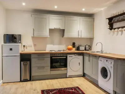 a kitchen with white cabinets and a washer and dryer at The Coach House in Bodmin