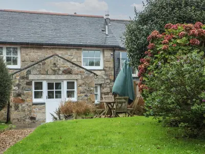 an old stone house with a garden and an umbrella at Trehan in St Ives