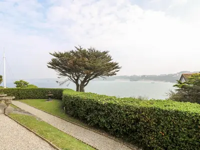 a park with a hedge and a tree and water at By The Sea in Newquay