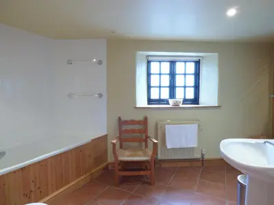 a bathroom with a tub and a chair and a sink at Meadow Cottage in Fowey