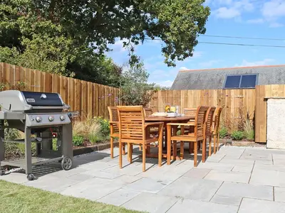 a patio with a table and chairs and a grill at Mill House, Boskensoe Barns in Falmouth