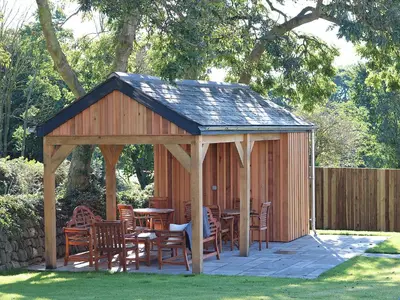 a wooden gazebo with wooden tables and chairs at The Stable, Boskensoe Barns in Falmouth