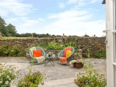 a patio with two chairs and a table and a stone wall at The Snug in Grampound
