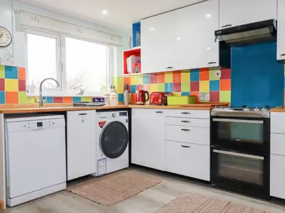 a kitchen with white cabinets and a washer and dryer at Daisy Cottage in Perranporth