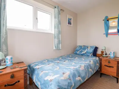a bedroom with a bed with a blue comforter and a window at Daisy Cottage in Perranporth