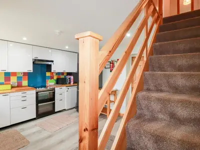 a staircase leading up to a kitchen with white cabinets at Daisy Cottage in Perranporth