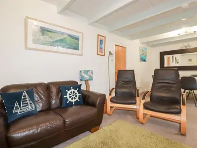 a living room with a leather couch and two chairs at Daisy Cottage in Perranporth