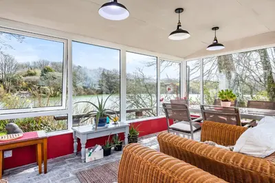 a living room with chairs and a table and windows at Tresowes Green Cottage in Helston