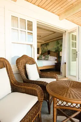 a porch with wicker chairs and a table and a bed at Tolcarne Beach Colonial Restaurant and Rooms in Newquay