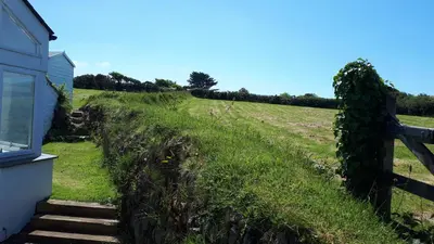 a grassy hill next to a house with a fence at Wrens Nook in St. Agnes