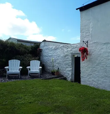 two white chairs sitting in a yard next to a building at Wrens Nook in St. Agnes