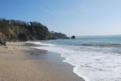 a beach with the ocean and rocks in the background at The Lodge, Polgooth in St Austell