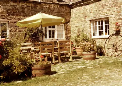 a table and chairs with an umbrella in front of a building at Old Newham Farm in Camelford