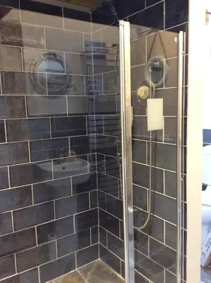 a shower in a bathroom with black tiles at Re-imagined Stone Barns in the Country Near the Coast in Padstow