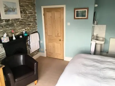 a bedroom with a bed and a chair next to a fireplace at Honeycombe House in Mevagissey