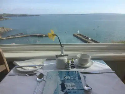 a table with a vase with a flower on a window at Honeycombe House in Mevagissey