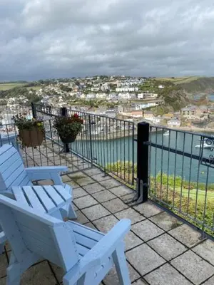 two white chairs sitting on a balcony overlooking the water at Honeycombe House in Mevagissey