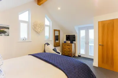 a bedroom with a bed and a tv and windows at The Lighthouse Penthouse, Studio and Holiday Home in St Ives